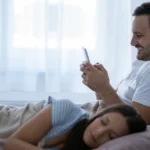A man texting another woman on his phone while his wife is sleeping, a form of micro-cheating